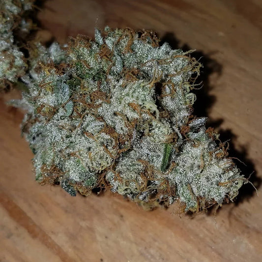 Close-up of frosty cannabis bud with orange hairs on a wooden surface